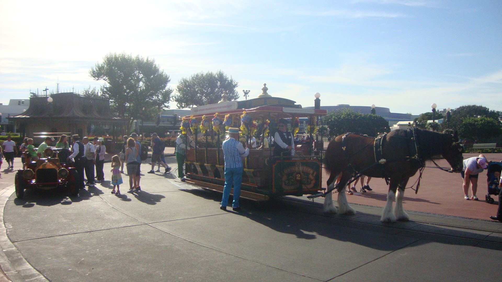 A garlanded horse-drawn streetcar and a vintage fire engine loading guests at Magic Kingdom in bright sunlight