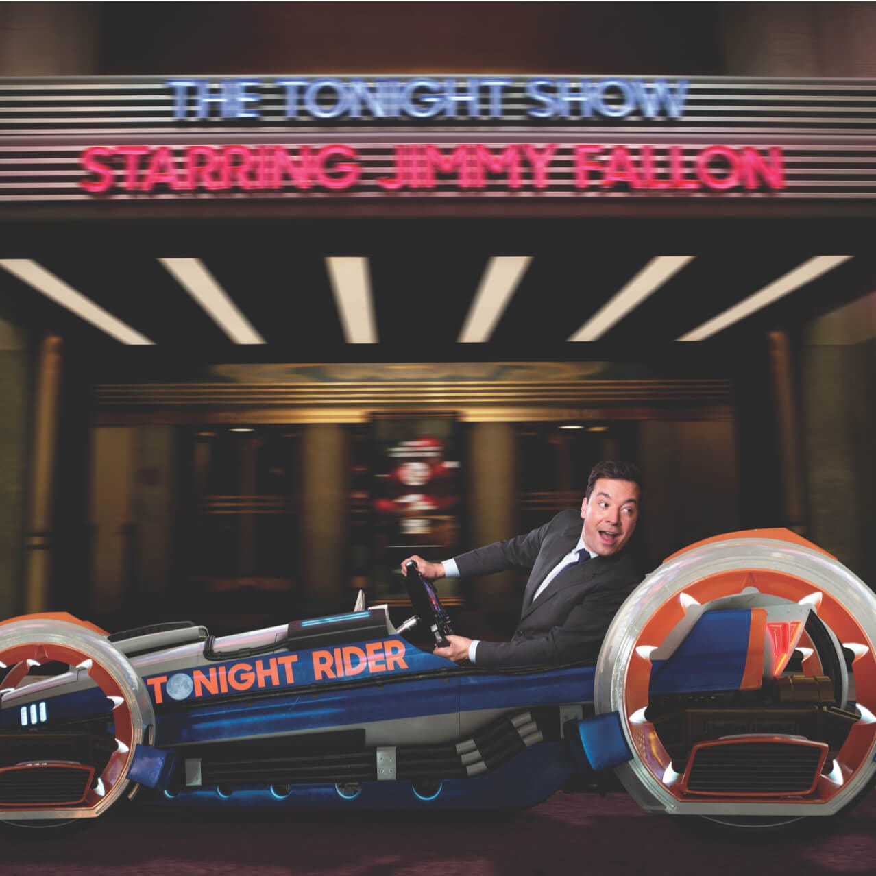 Jimmy Fallon seated in the Tonight Rider vehicle in front of The Tonight Show marquee in promotional art for Race Through New York Starring Jimmy Fallon