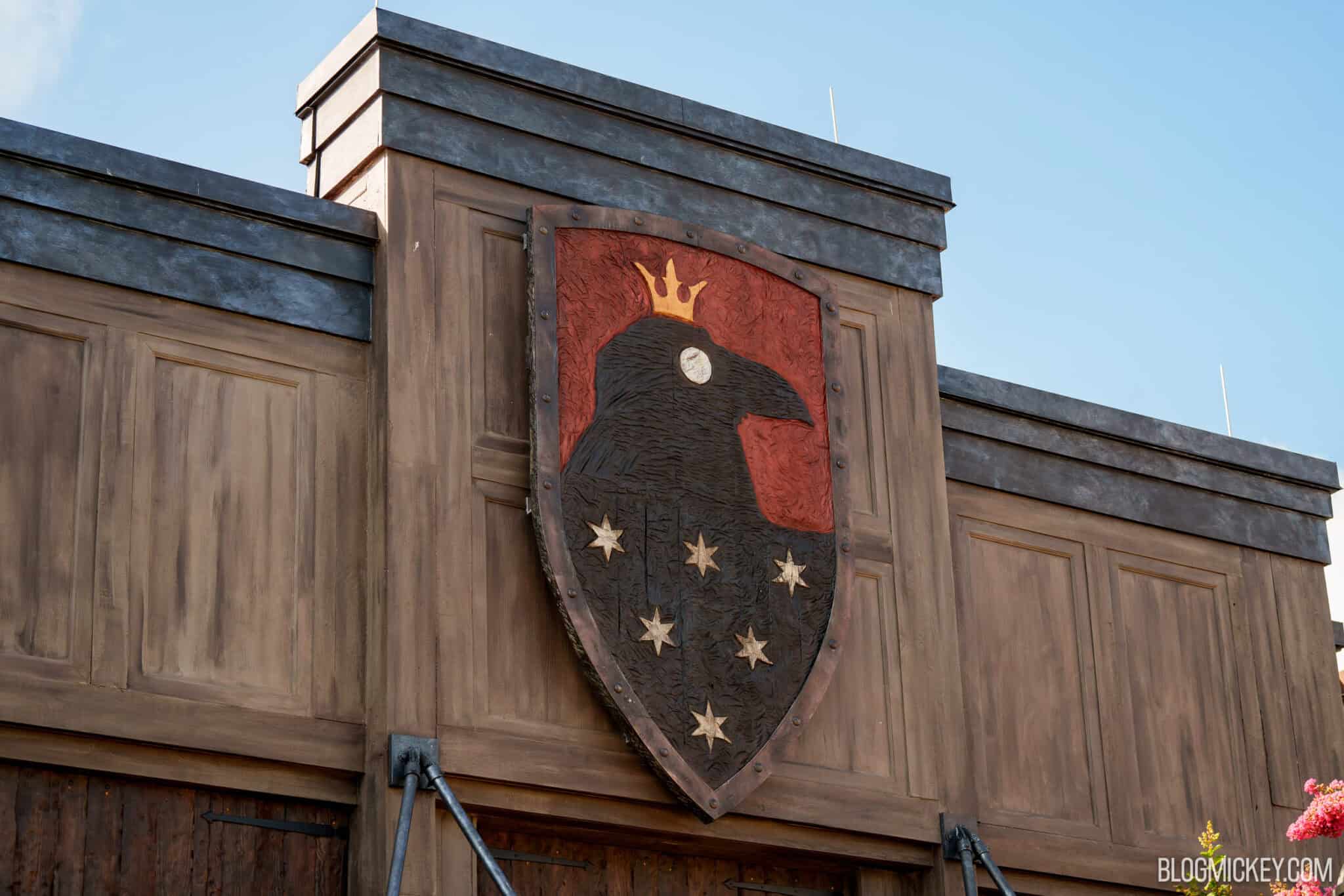 A carved crest of a crowned black raven with six white stars, on a red and black shield mounted high on the facade of the Six Ravens building