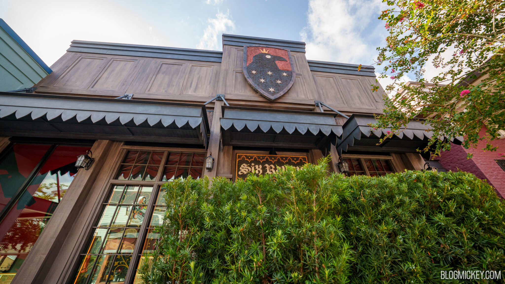 Looking up at the Six Ravens facade, showing the blackletter sign, scalloped black awnings and the raven crest mounted above them