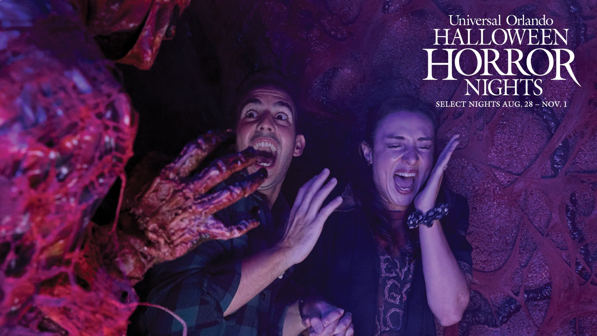 Official Halloween Horror Nights key art showing two guests screaming inside a red and purple fleshy tunnel as a clawed hand reaches for them, with the Universal Orlando Halloween Horror Nights logo and the dates Select Nights Aug. 28 to Nov. 1.