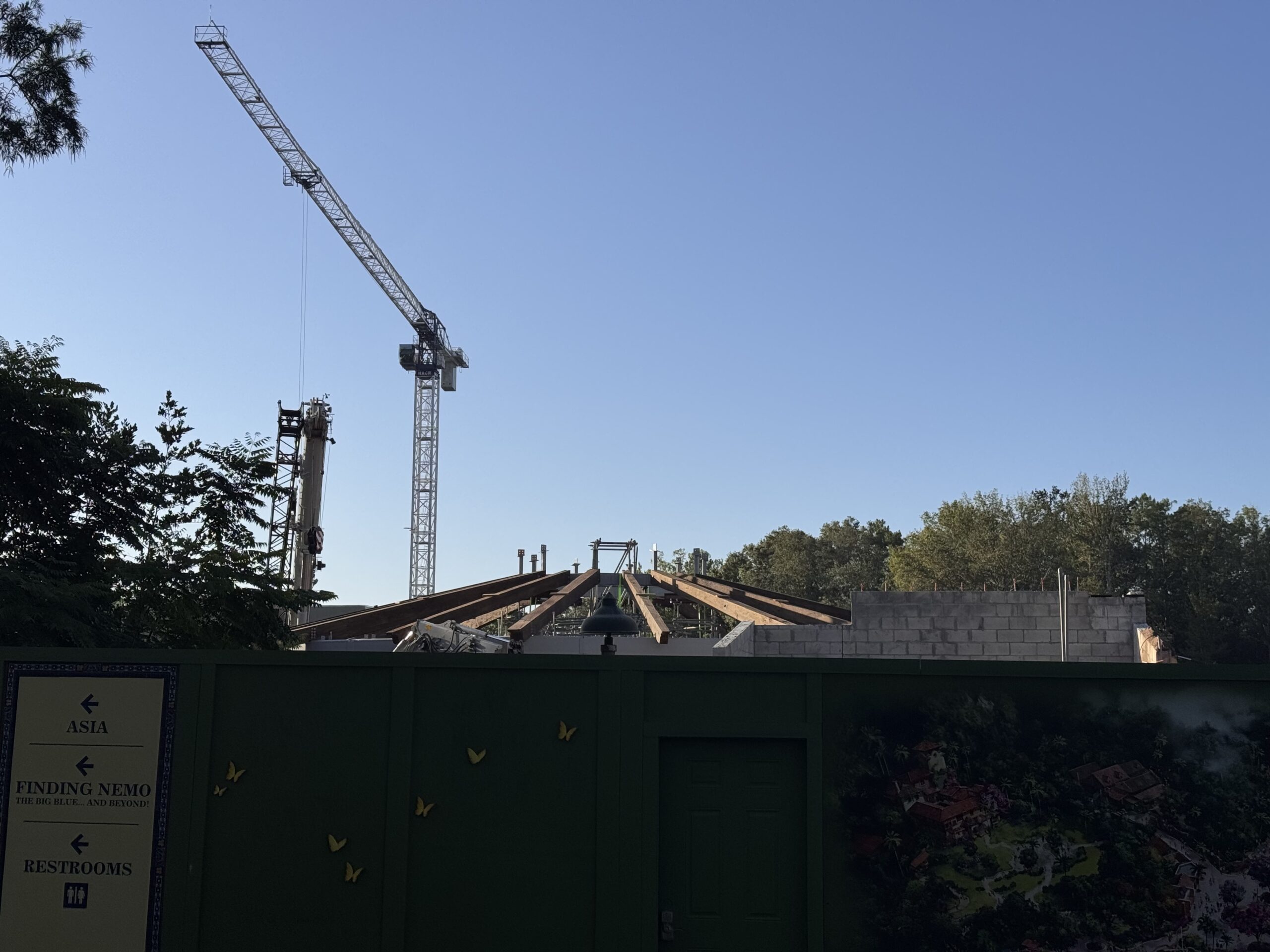 Angled wooden roof beams radiate from the center of the Tropical Americas carousel over its block walls, with a tower crane behind the construction wall