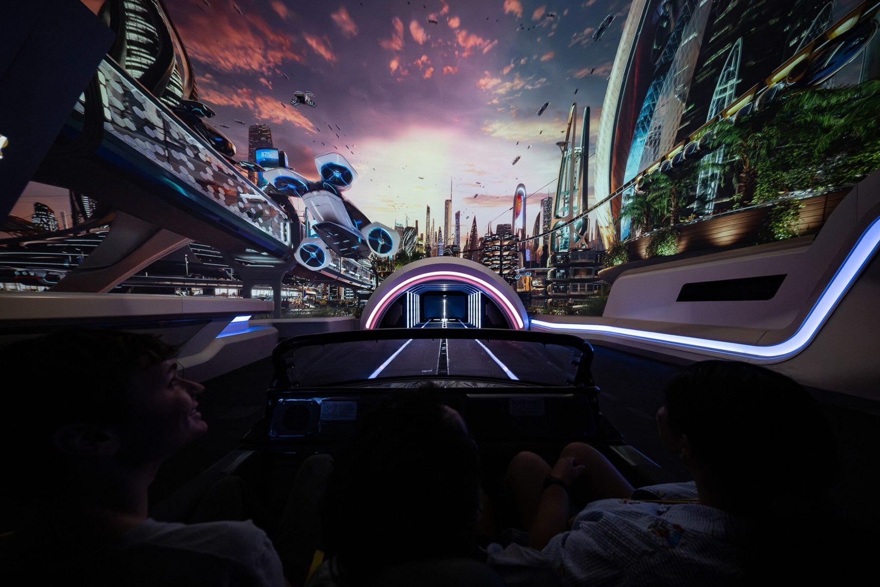 View from inside a Test Track ride vehicle looking down a roadway toward a pink lit archway and tunnel, with a futuristic city skyline projected on the walls around it