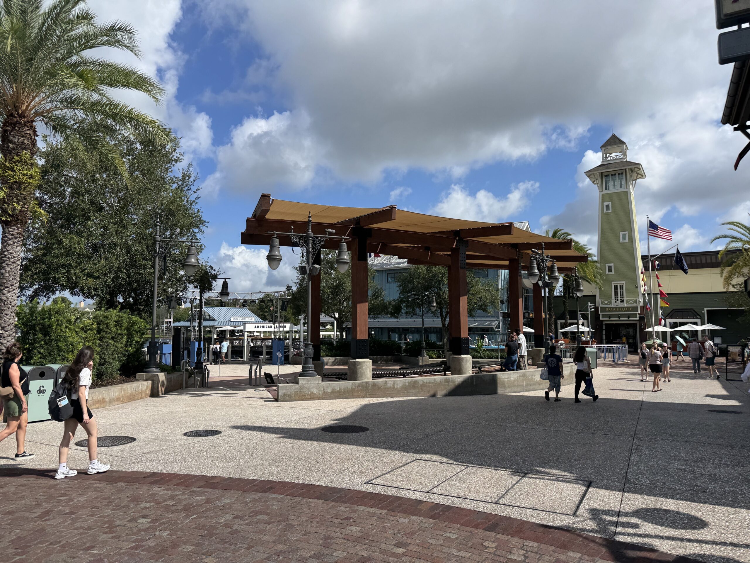 Guests walking through the Disney Springs plaza past the reopened Waterview Park, its tan canopy in place and no construction walls around it