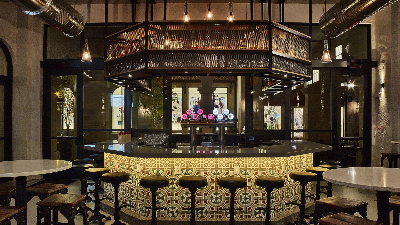 The tiled central bar at The Polite Pig, lit by hanging bulbs with liquor bottles racked overhead and stools around the counter