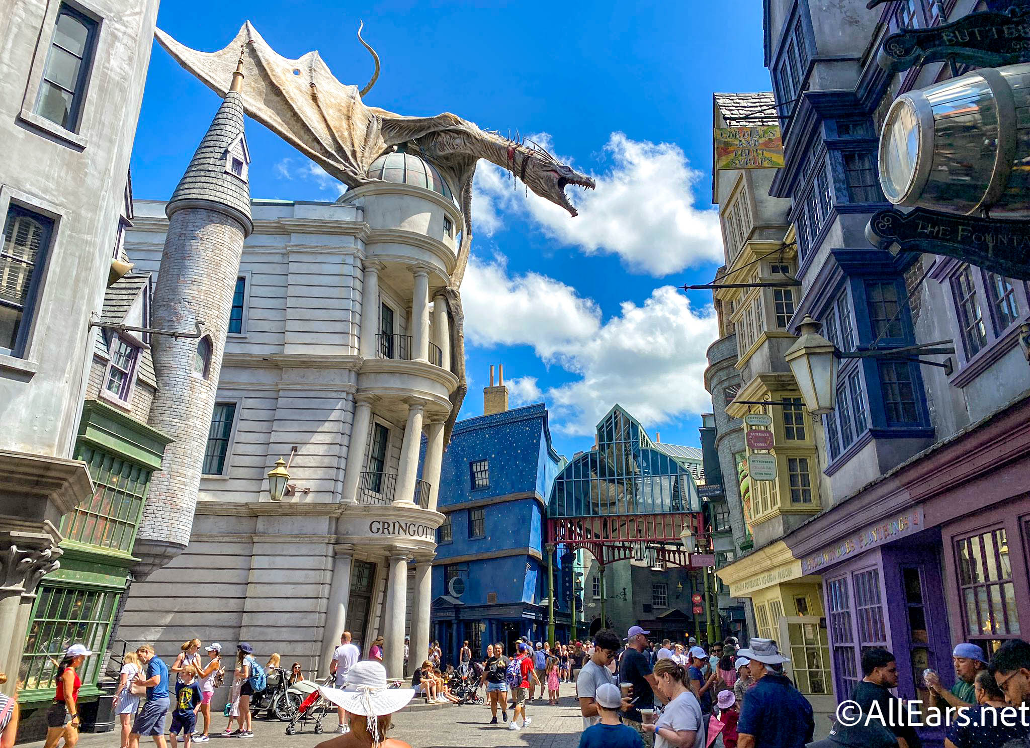 Diagon Alley at Universal Studios Florida on a bright day, with the Ukrainian Ironbelly dragon perched atop the white Gringotts bank building and crowds filling the street below