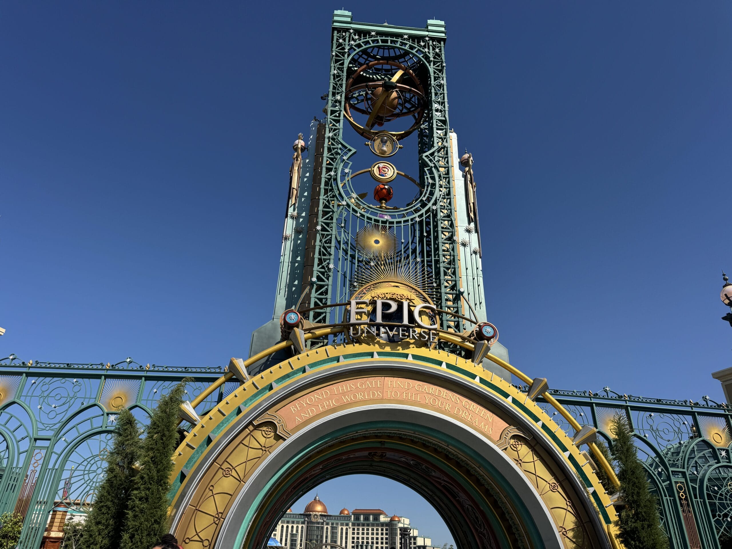 The ornate metal entrance arch at Universal Epic Universe against a clear blue sky, with the park logo mounted at its center