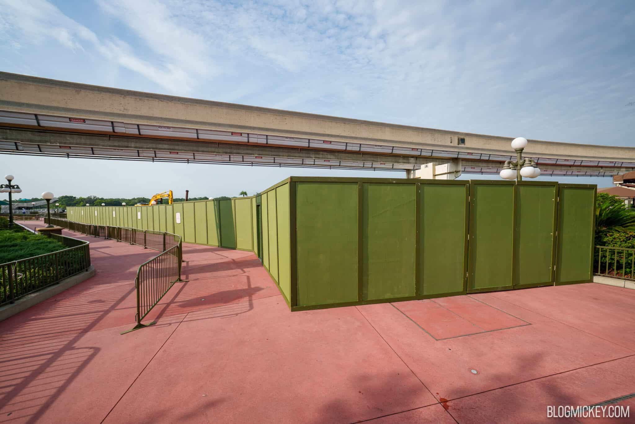 Green construction walls running beneath the Walt Disney World monorail beam along a pink guest walkway.