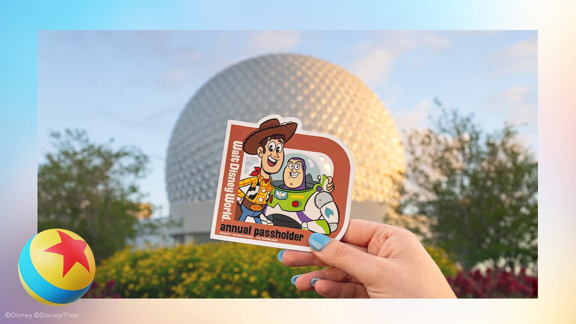 A hand holding a Walt Disney World annual passholder magnet showing Woody and Buzz Lightyear, with Spaceship Earth blurred behind it