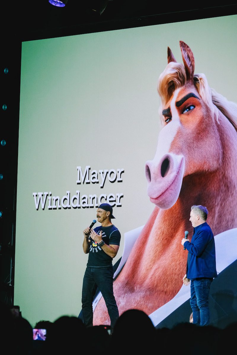 Patrick Warburton on stage with another speaker in front of a large projected image of Mayor Winddancer, the horse mayor from Zootopia 2, at Destination D23 2025