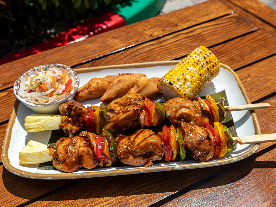 A plate of grilled chicken skewers with bell peppers and pineapple, served with fried dough and dipping sauce