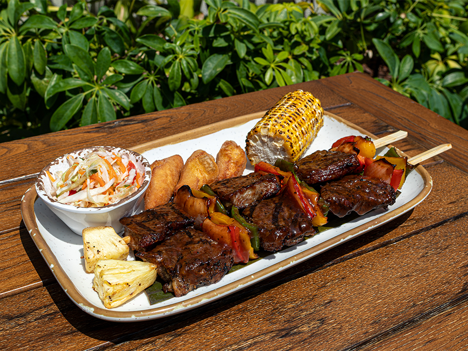 A plate of grilled New York steak skewers with peppers and pineapple alongside fried sides