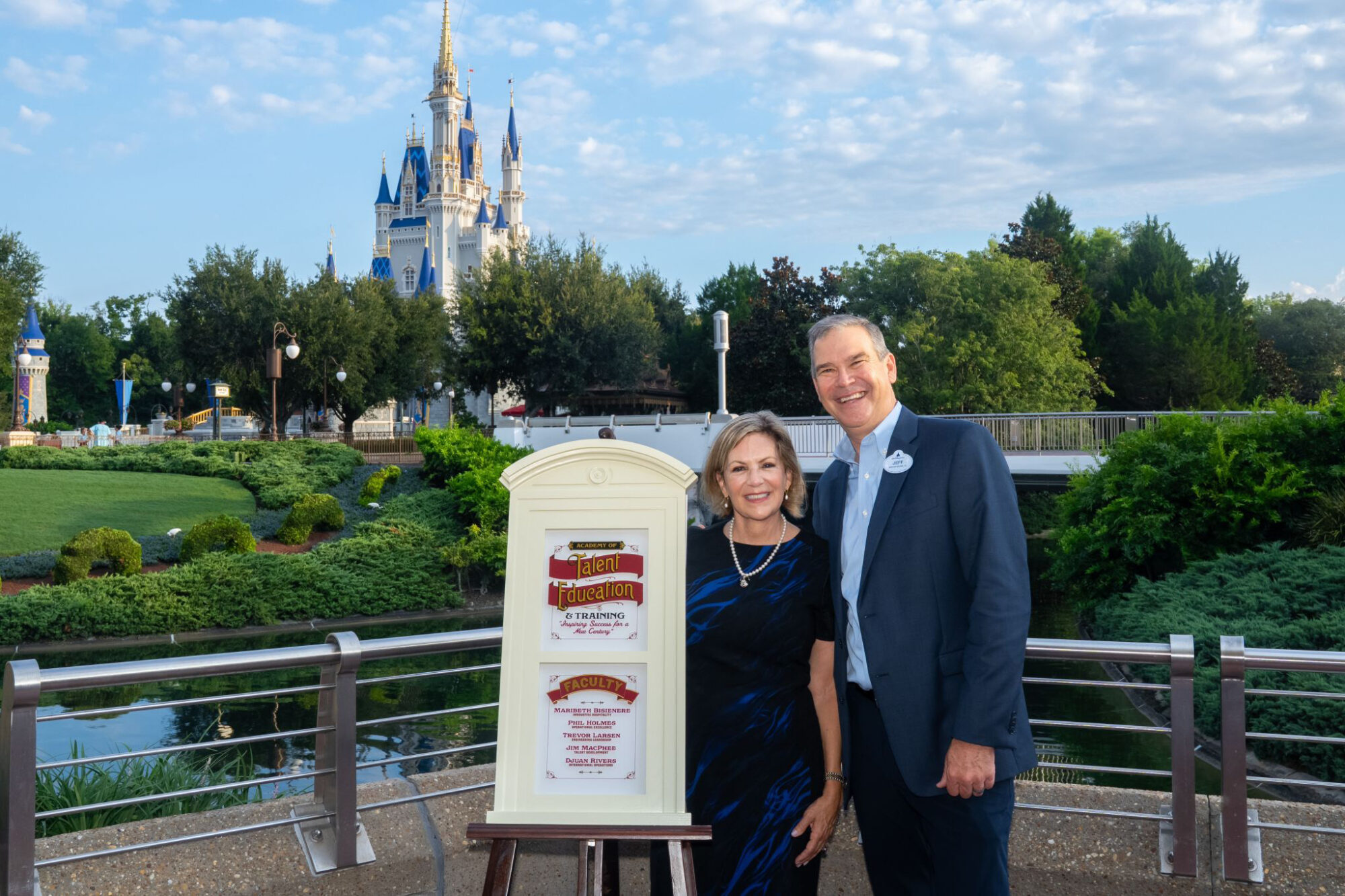 Maribeth Bisienere and Jeff Vahle stand together beside a replica window on an easel with Cinderella Castle in the background