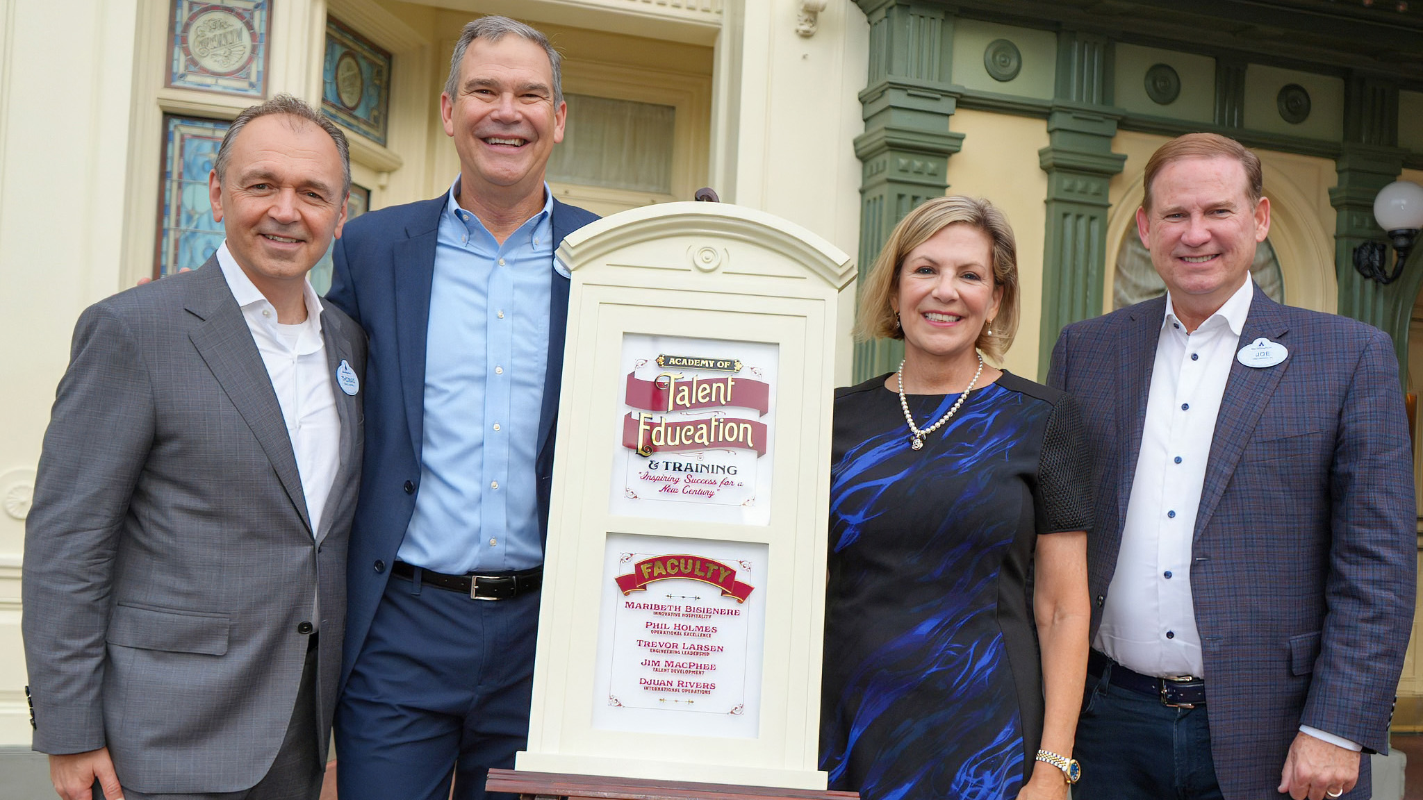 Four Disney executives stand on either side of a freestanding replica of Bisienere's window pane mounted on an easel outside a Main Street building
