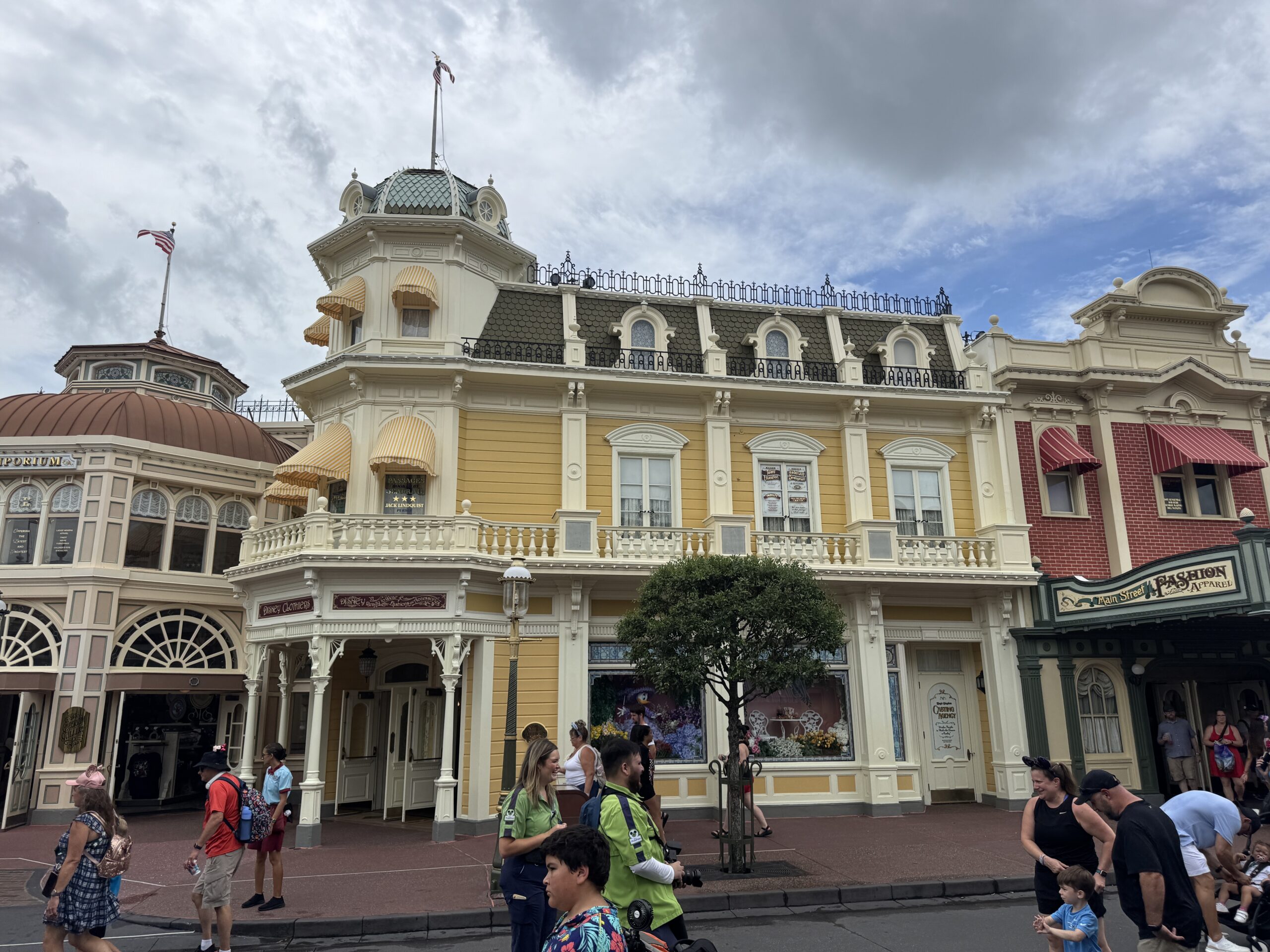 Wide view of a yellow Main Street, U.S.A. building with the Casting Agency door at street level and painted windows on the second floor, with the Emporium at left and Main Street Fashion and Apparel at right
