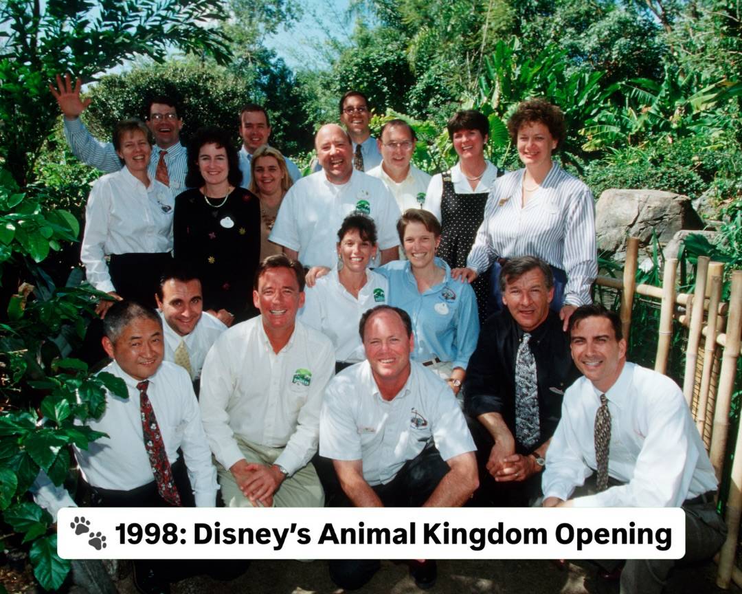 A 1998 group photo of about twenty Disney employees posed in lush foliage, with a white caption bar reading 1998: Disney's Animal Kingdom Opening