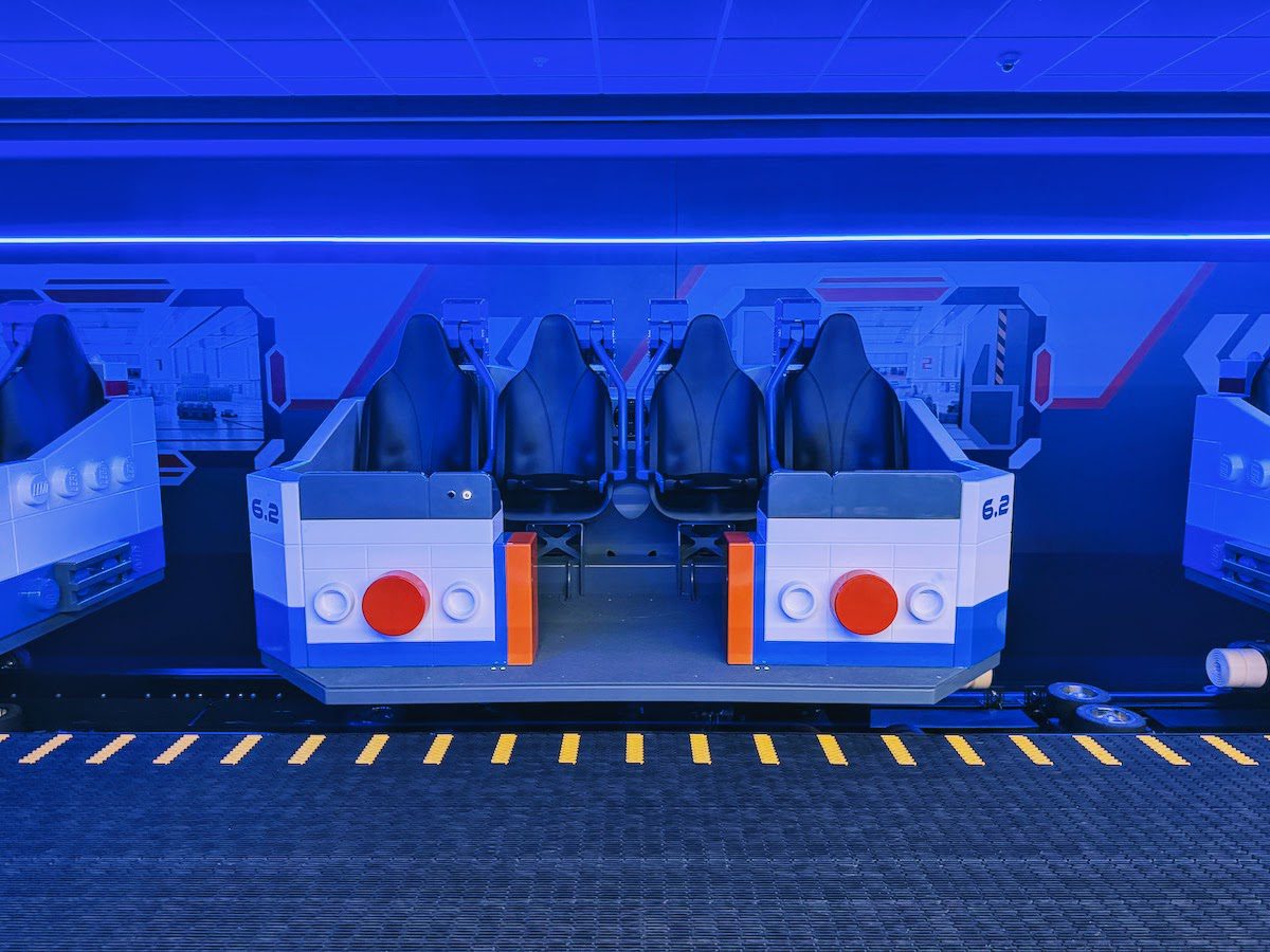 A Galacticoaster ride vehicle sitting in its loading station, lit in deep blue, with black bucket seats and white and blue brick styled bodywork.