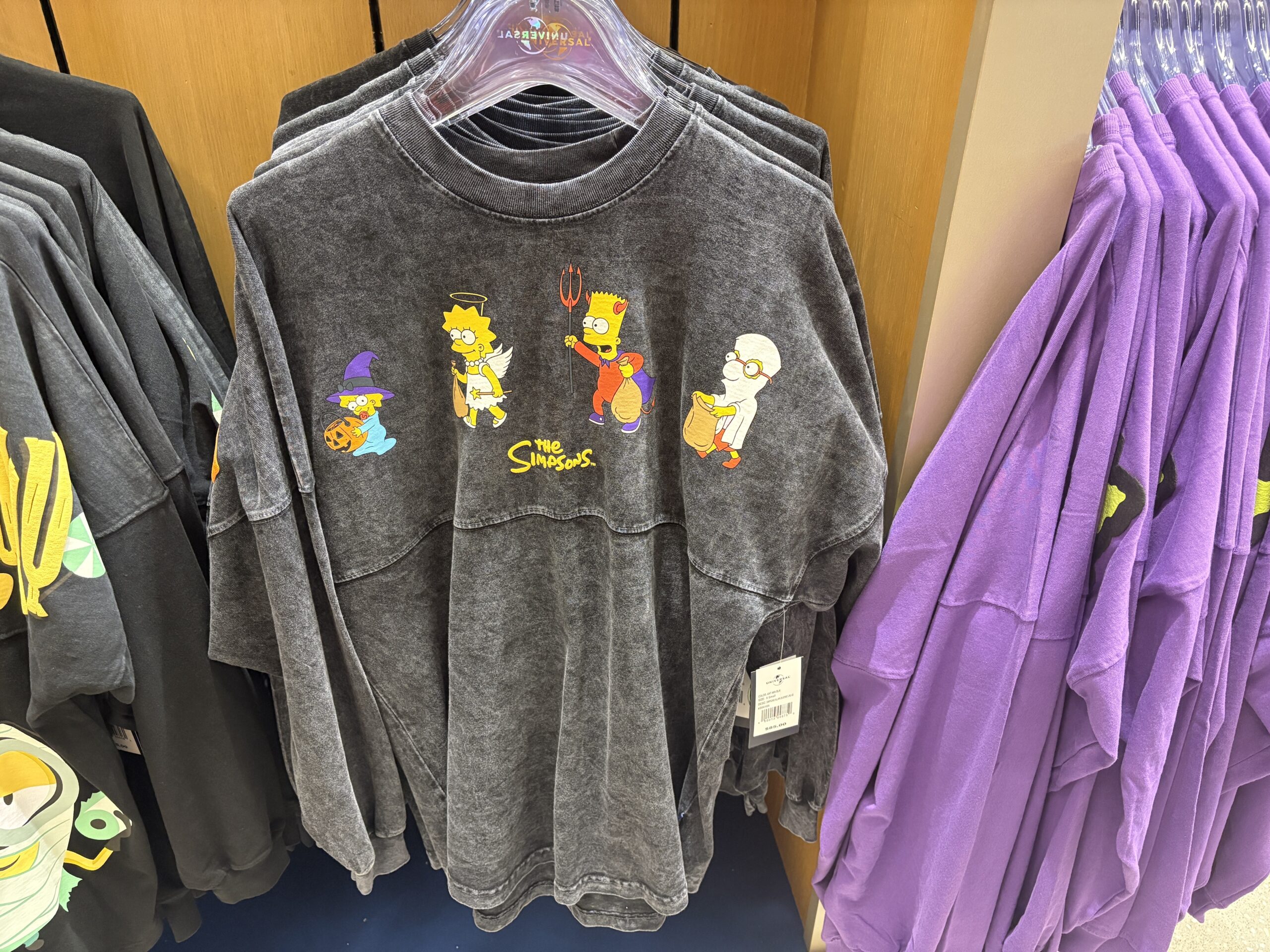 A charcoal acid wash Spirit Jersey with Maggie dressed as a witch, Lisa as an angel, Bart as a devil and Milhouse as a mummy printed across the chest above The Simpsons logo.