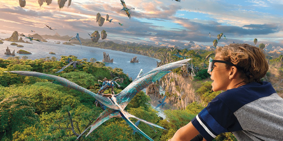 Promotional image for Avatar Flight of Passage showing a guest in 3D glasses watching a Na'vi rider on a banshee fly over the forests, water and floating rocks of Pandora
