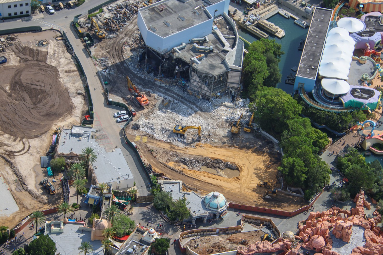Aerial view of Universal Islands of Adventure showing a large cleared expanse of graded earth on the left, the partly demolished Poseidon's Fury show building in the center, and Seuss Landing to the right across the water.