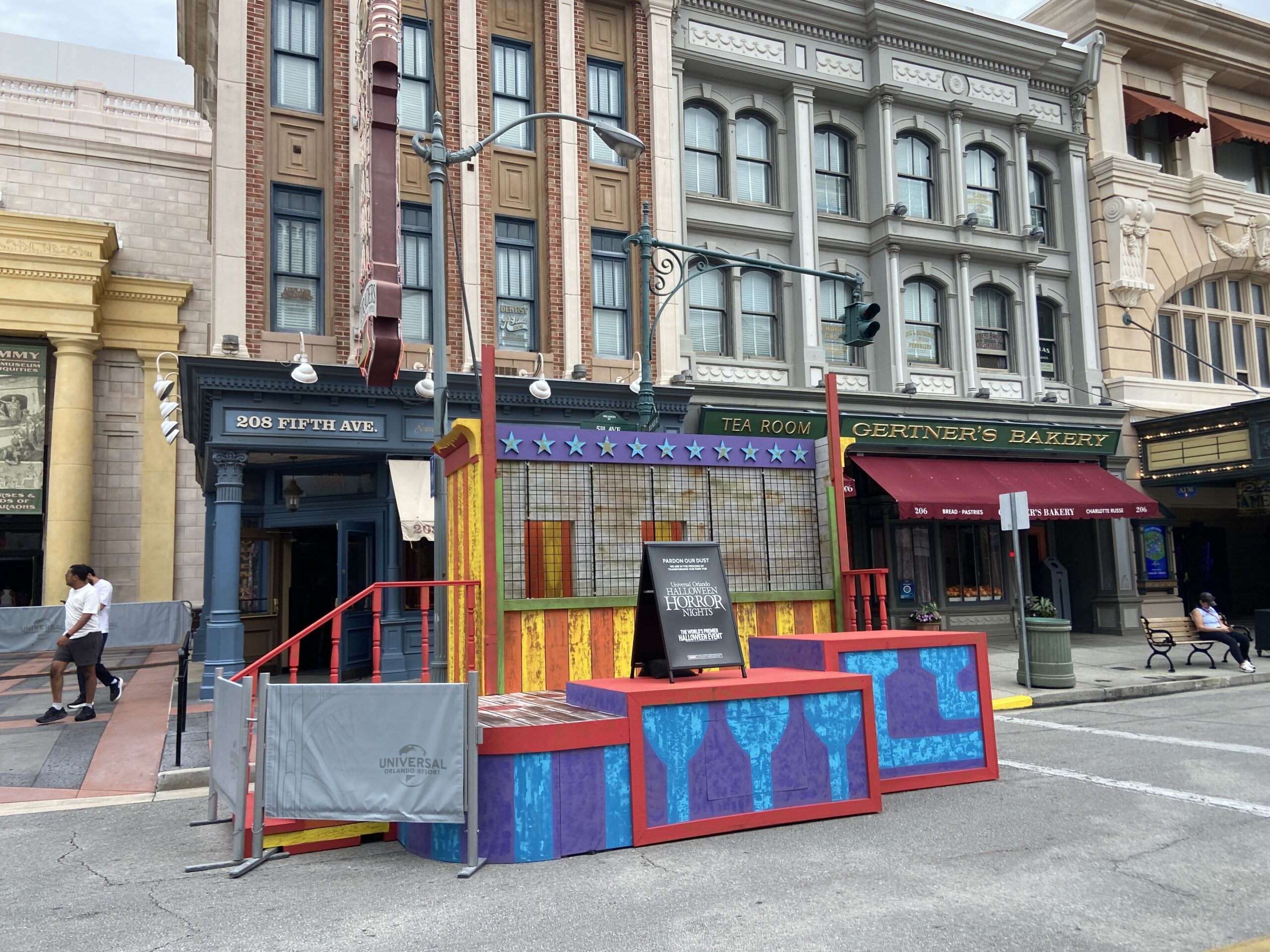 A rainbow striped stage with a purple valance of pale blue stars and a wire mesh caged back compartment, standing outside the 208 Fifth Avenue storefront beside Gertner's Bakery