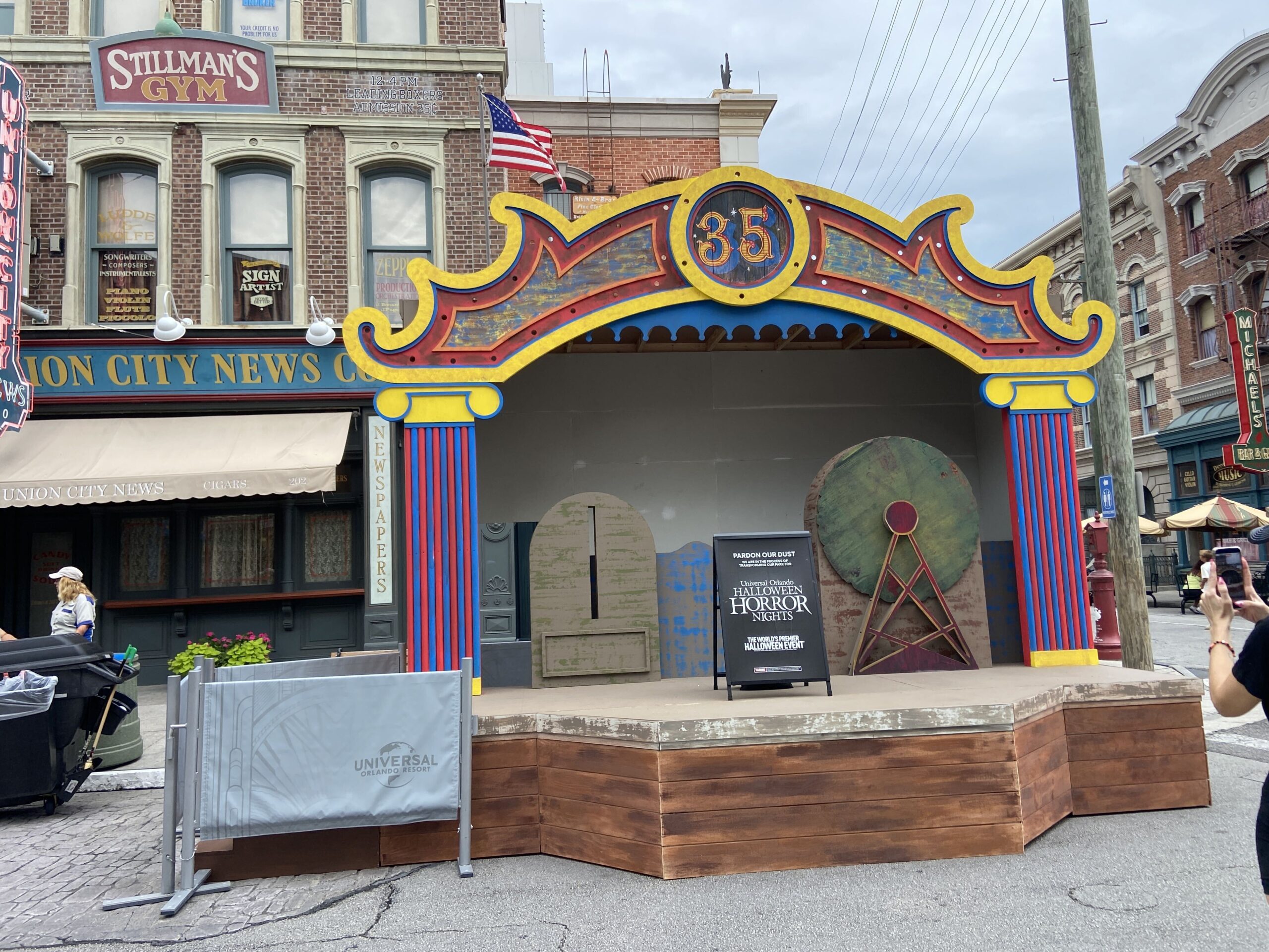 A carnival stage with a red, blue and yellow arch bearing the number 35, set on a wooden platform beside the Union City News storefront