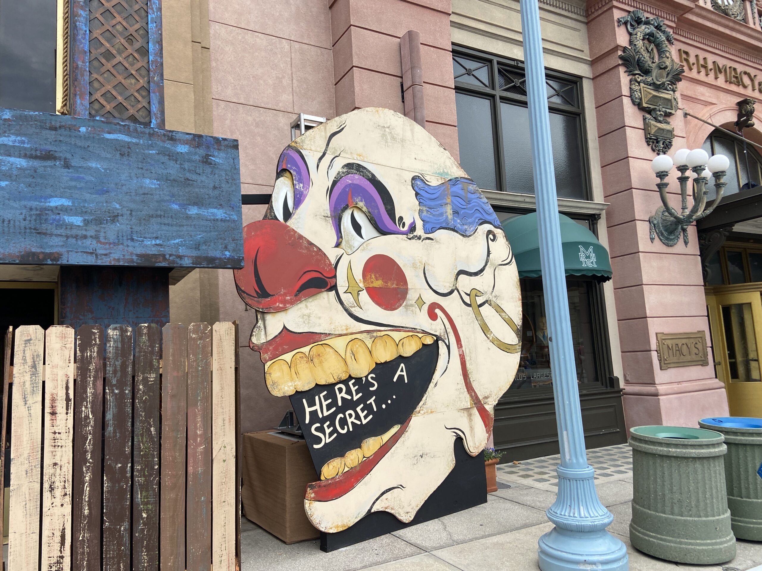 Close view of the painted clown face cutout showing purple eyeshadow, a red nose, yellow teeth and a black open mouth lettered Here's a secret