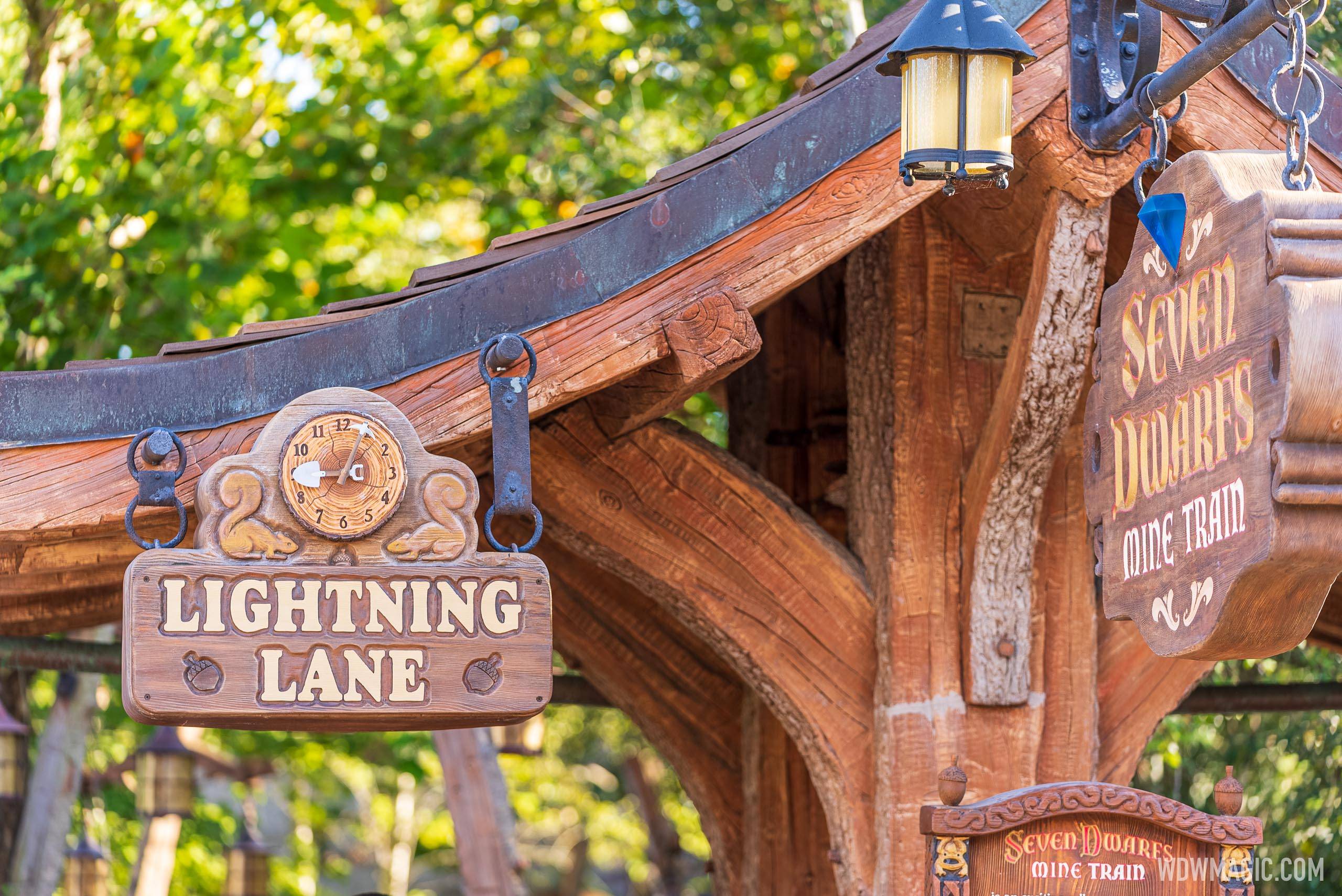 A carved wooden Lightning Lane sign with a clock face and squirrels hanging beneath the Seven Dwarfs Mine Train entrance canopy.