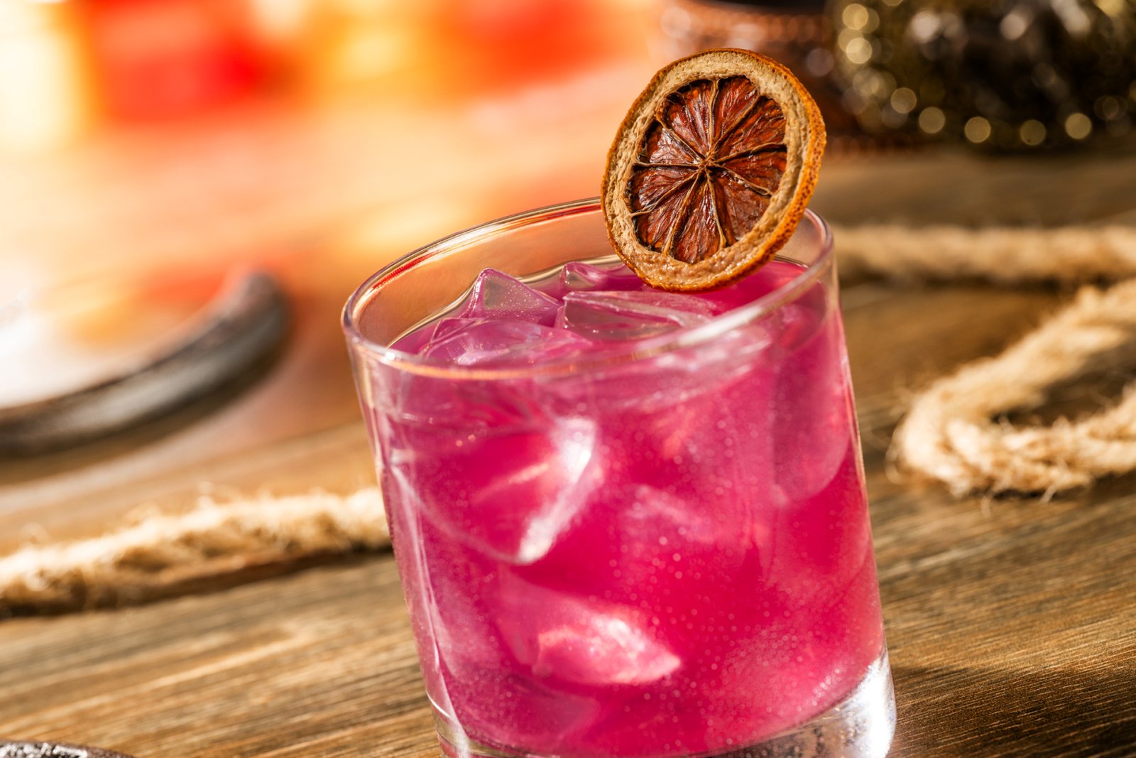 A deep magenta prickly pear margarita on the rocks in a rocks glass, garnished with a dried lime wheel