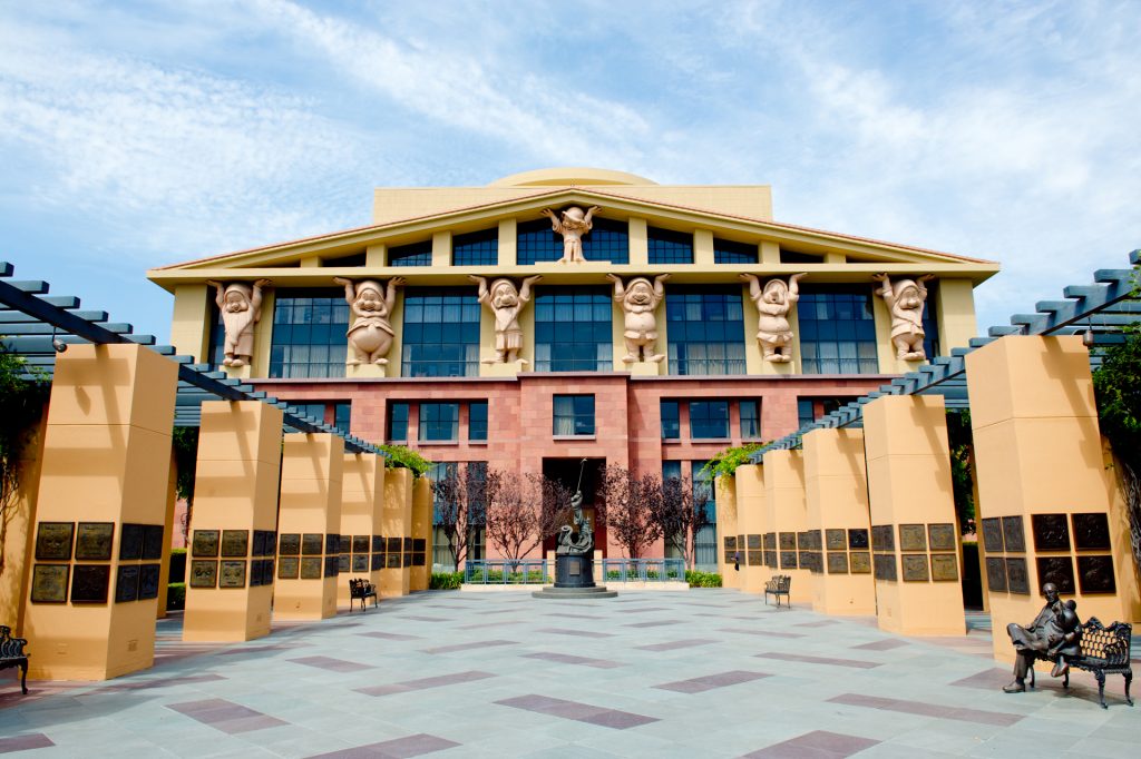 The Team Disney building in Burbank, its facade lined with giant Seven Dwarfs figures holding up the roofline, seen across the Legends Plaza courtyard.