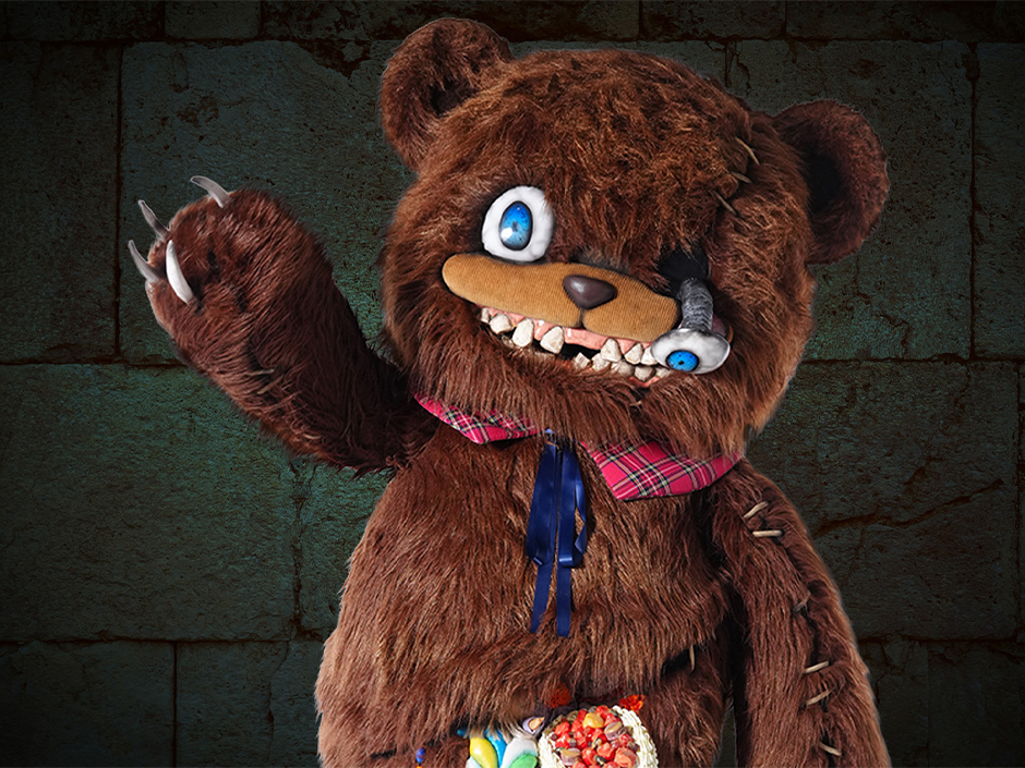 Official Universal character art of HamiKuma, a brown teddy bear with stitched seams, long claws, one large blue eye and a second eye dangling loose beside his muzzle, a plaid bow tie and candy spilling from a torn belly