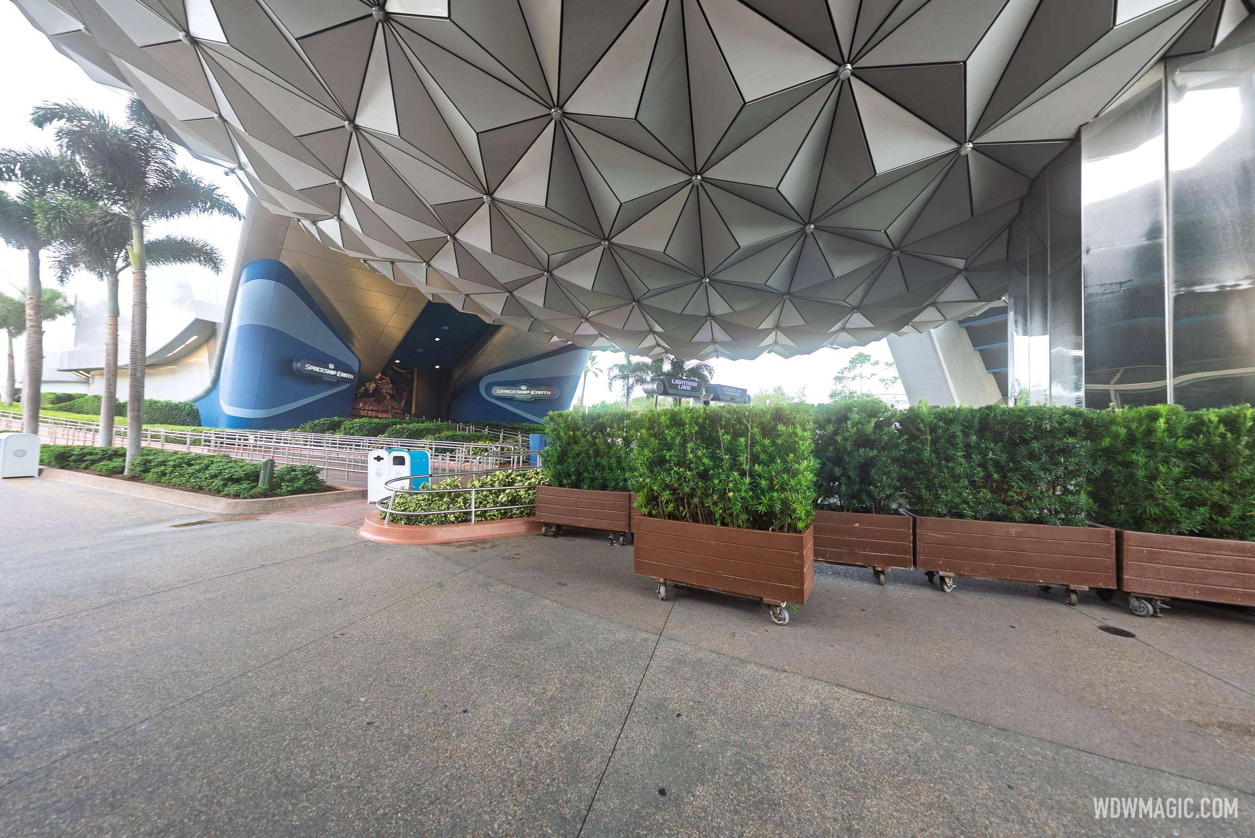 The Spaceship Earth ride entrance at EPCOT, with two dark oval marquee signs reading Spaceship Earth on the blue walls flanking the entrance under the sphere, an empty switchback queue behind metal rails, and Lightning Lane and Standby signs on a post beyond the queue.