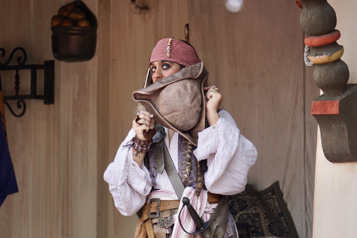 Captain Jack Sparrow holding a large leather pirate hat up in front of his face in Adventureland at Magic Kingdom.