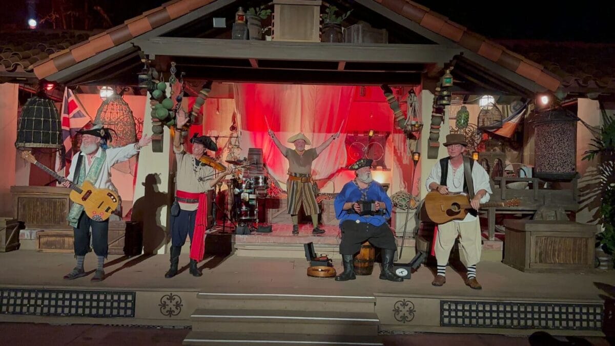 The five-piece Rusty Cutlass pirate band performing on the Adventureland stage at night during Mickey's Not-So-Scary Halloween Party, lit in red.