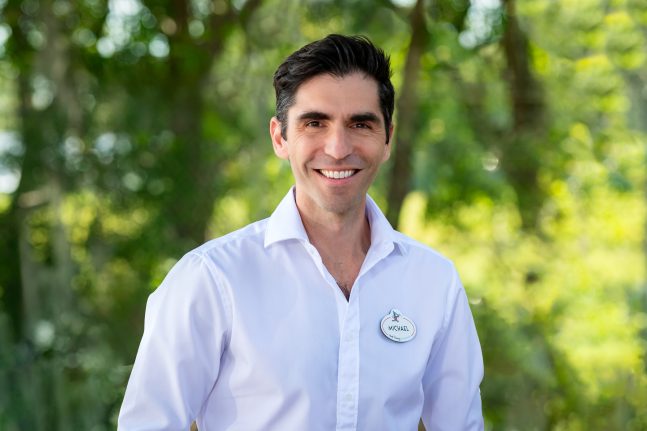 Portrait of Imagineer Michael Hundgen smiling outdoors in a white shirt with a Disney name tag