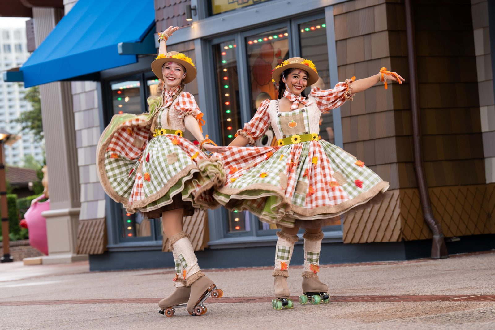 Two Disney Springs performers on roller skates wearing gingham scarecrow dresses, straw hats with sunflowers and painted faces, spinning outside a storefront