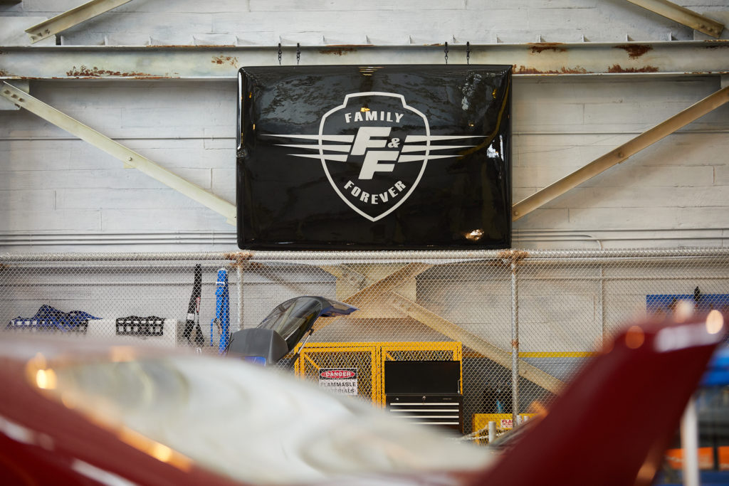 A black banner reading FAMILY F and F FOREVER inside a shield, hanging in the Supercharged garage