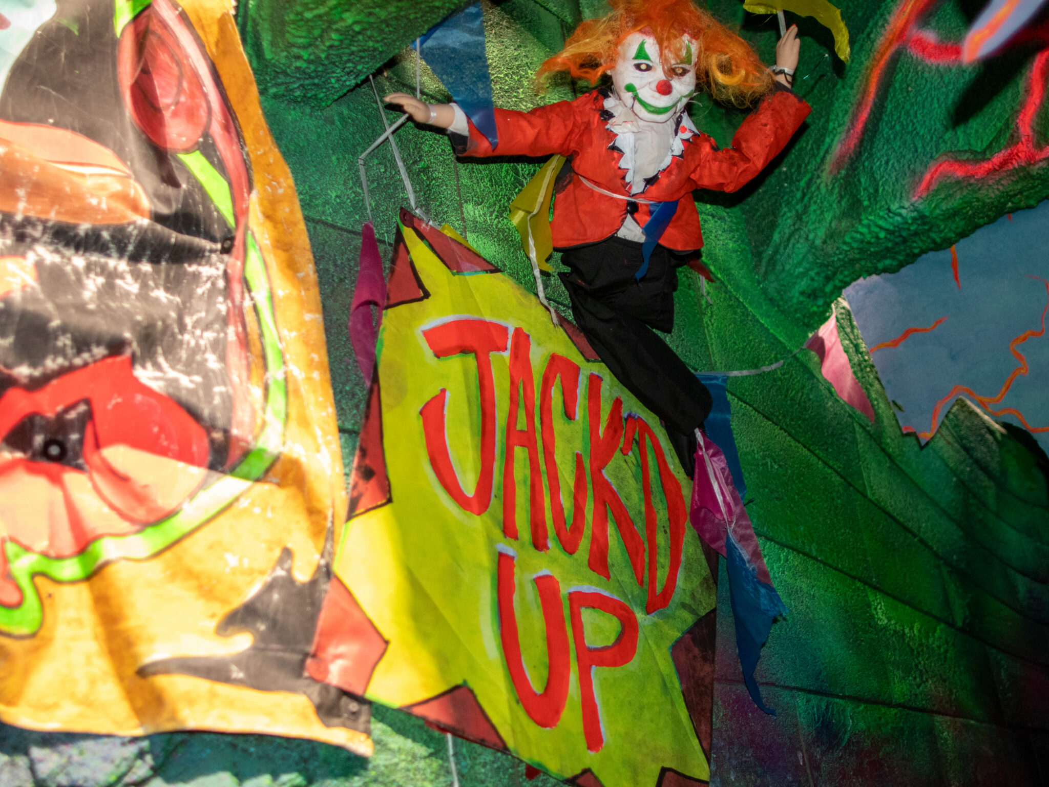 A hand-painted yellow banner reading JACK'D UP hangs beside a clown marionette suspended on strings