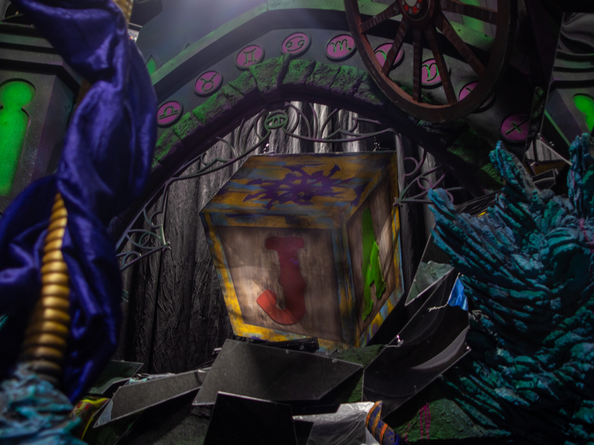 A wooden box painted with a red letter J hangs inside a stone archway ringed with pink zodiac symbols
