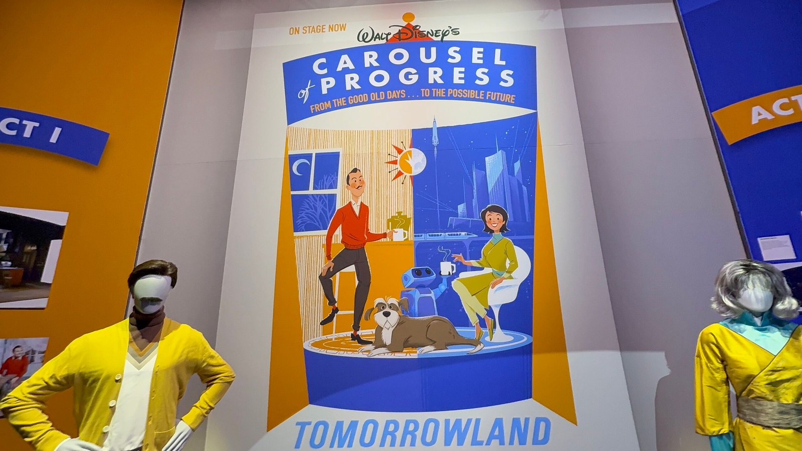 A new Carousel of Progress attraction poster mounted on a wall, flanked by two costume mannequins on plinths