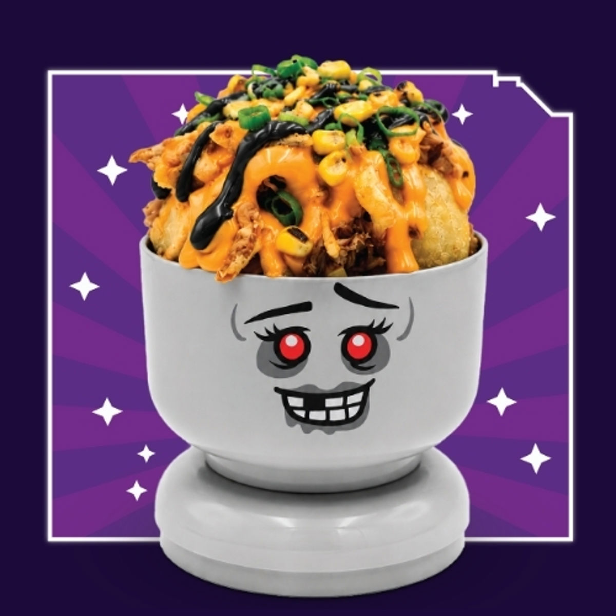 A white and grey LEGO zombie Minifigure head bowl on a stud base, printed with red eyes and a wide grin of square white teeth, heaped with twisted fries under orange cheese sauce, pulled pork, corn, green onions and a black aioli drizzle, on a purple starburst background.