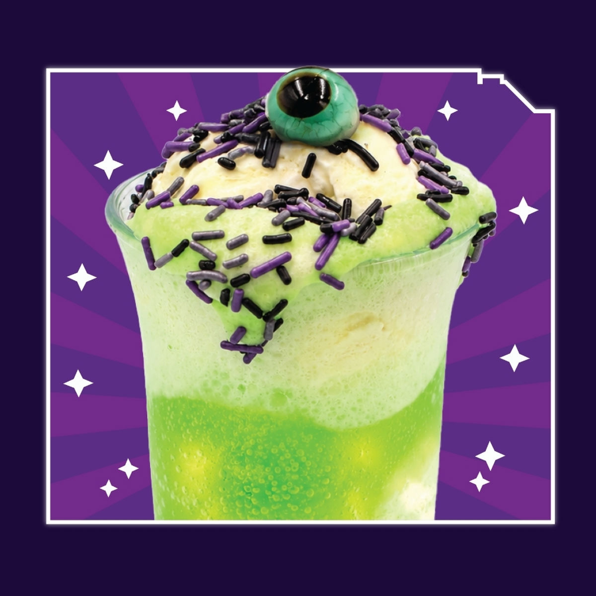 A tall clear glass of bright green soda topped with a scoop of vanilla ice cream covered in purple, black and silver sprinkles, with a glossy green and black gummy eyeball resting on top, on a purple starburst background.