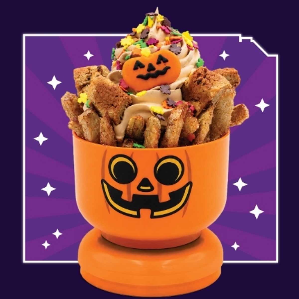 An orange LEGO jack-o-lantern Minifigure head bowl on a stud base, filled with apple fries and cookie pieces, topped with a tall swirl of tan pumpkin soft serve, autumn leaf sprinkles and an orange pumpkin-shaped cookie, on a purple starburst background.