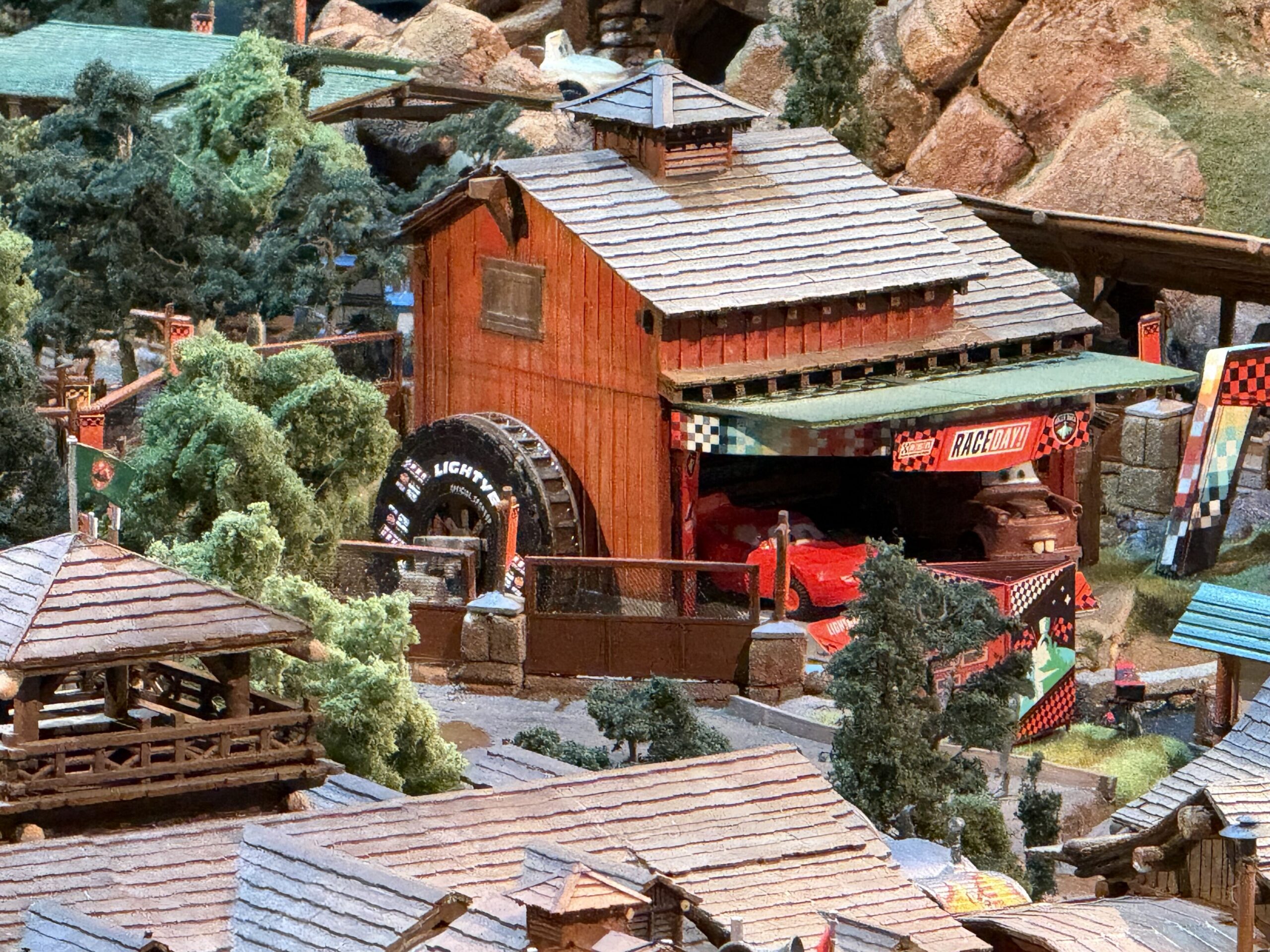 A rust red mill building in the model with a shingled roof and a water wheel made from a large black tire lettered LIGHTYEAR