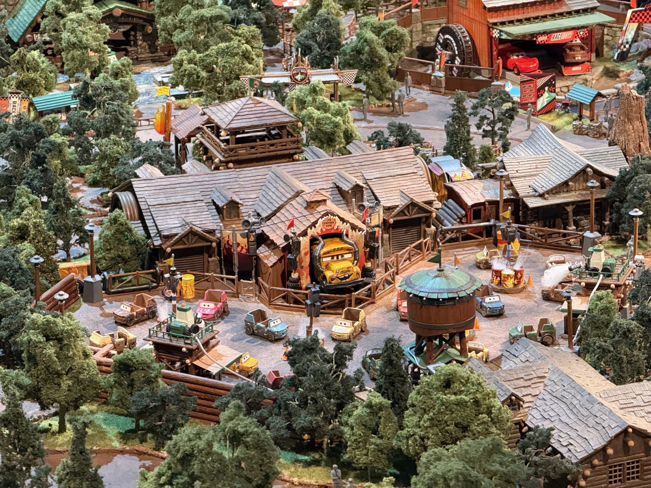 Overhead view of the Piston Peak model showing a yellow school bus figure with horns inside a flame painted opening, with small Cars character figures parked on the plaza in front
