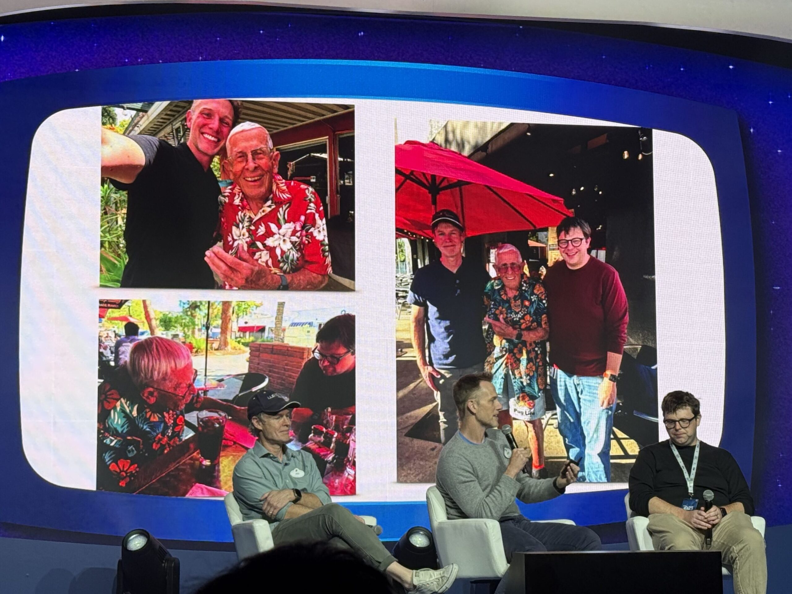 A D23 panel stage with a screen behind it showing three photos of Imagineers visiting an older man in a Hawaiian shirt outdoors at a restaurant