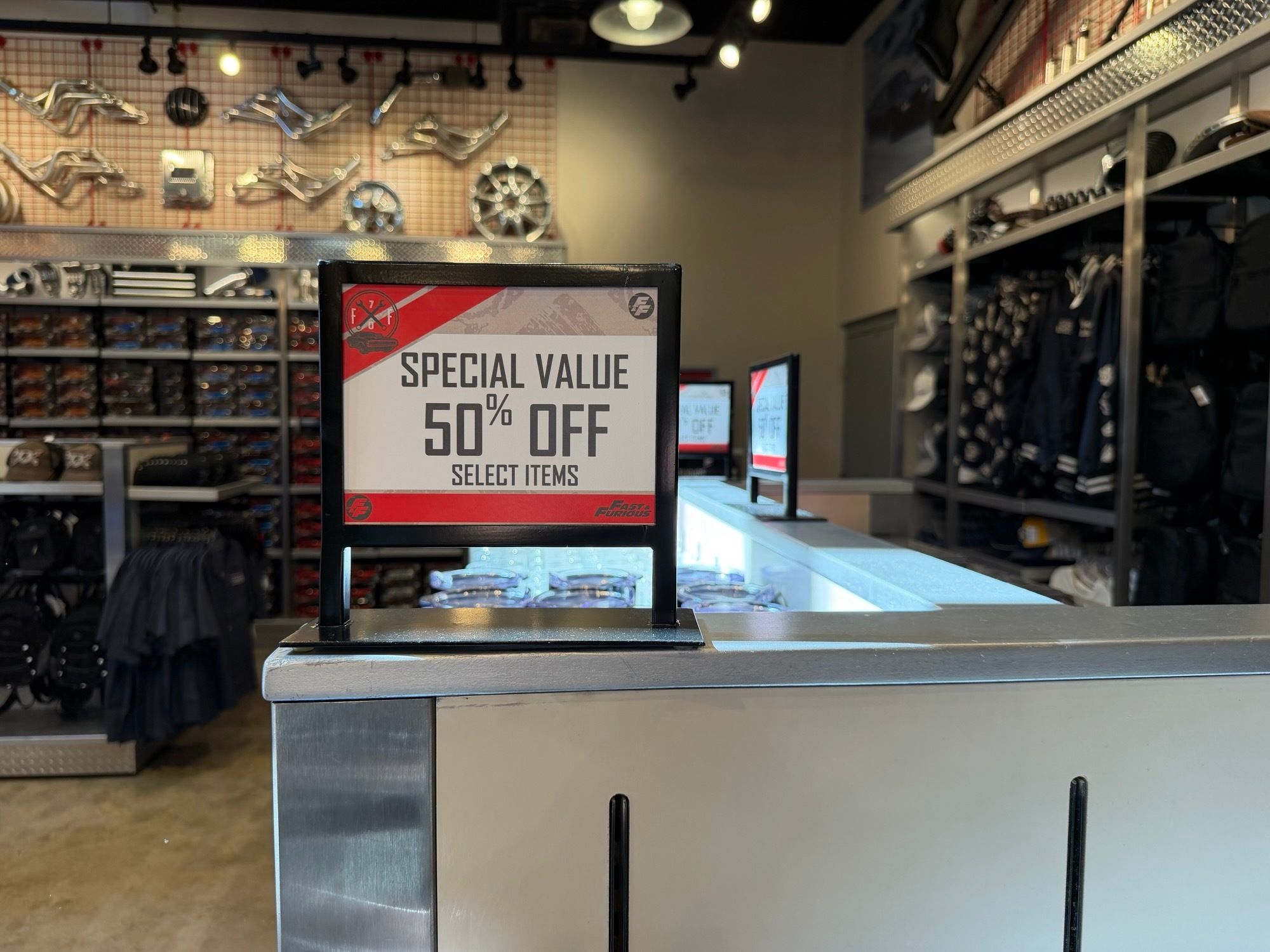 A countertop sign inside a Fast and Furious themed gift shop reading Special Value 50 percent off select items, with more of the same signs further down the counter