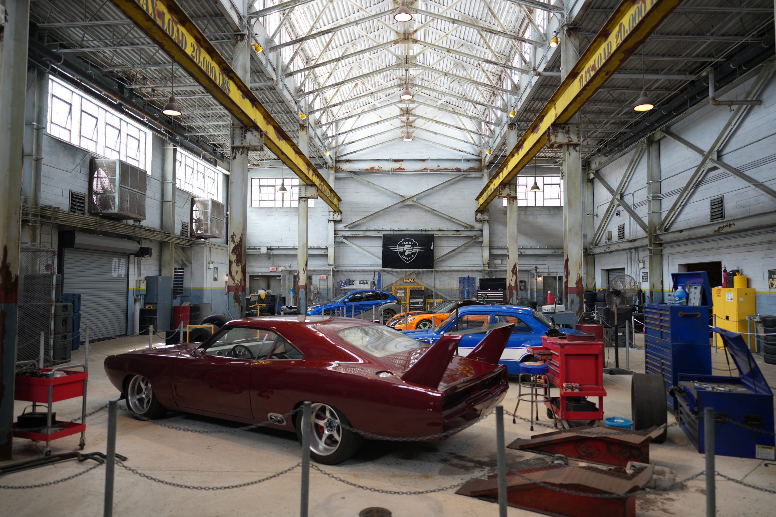 The indoor garage set at Fast and Furious Supercharged in Universal Studios Florida, with four hero cars parked under yellow overhead cranes and a Family Forever banner on the back wall