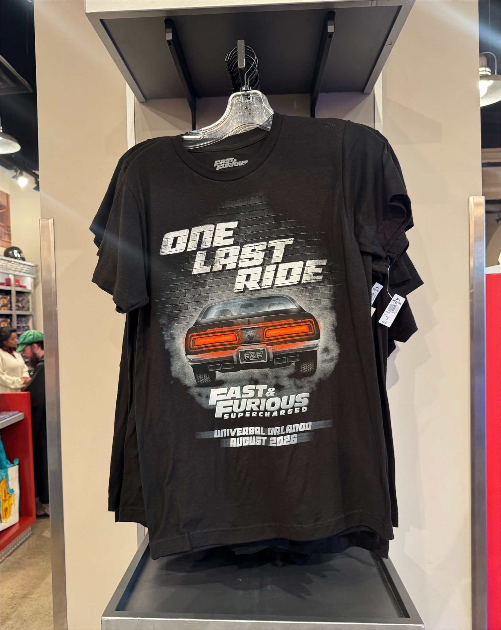 A black t-shirt printed with One Last Ride and Fast and Furious Supercharged artwork, displayed on a store rack
