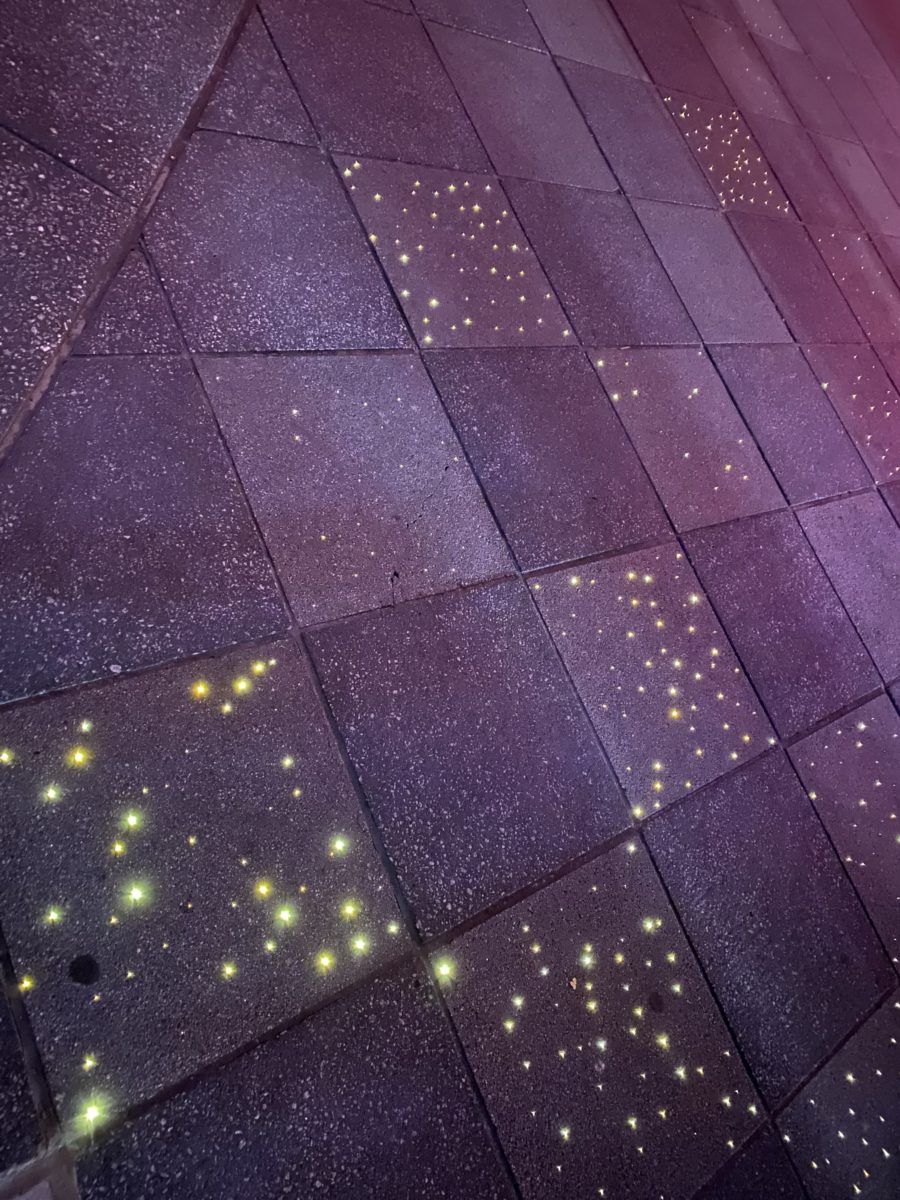 Close view of old Future World pavement at night, with clusters of tiny warm white pinpoint lights embedded in dark speckled paving squares